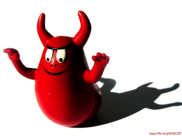 A red toy devil against a white background with a stark shadow