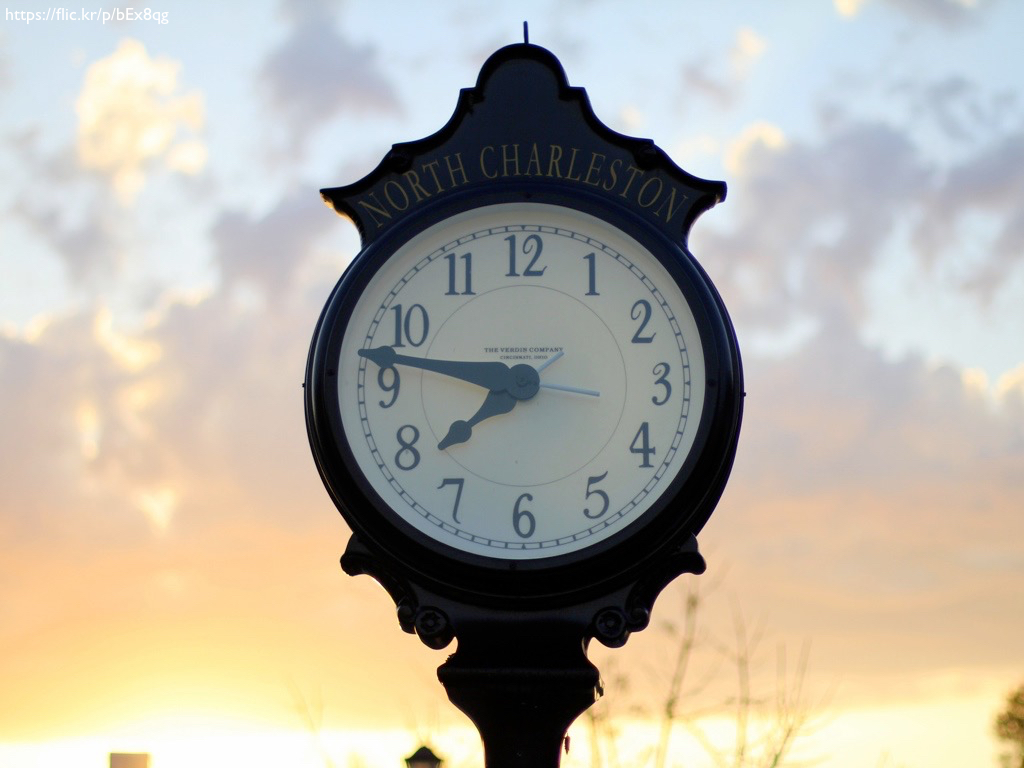 A clock on a metal stand, against a sunset.