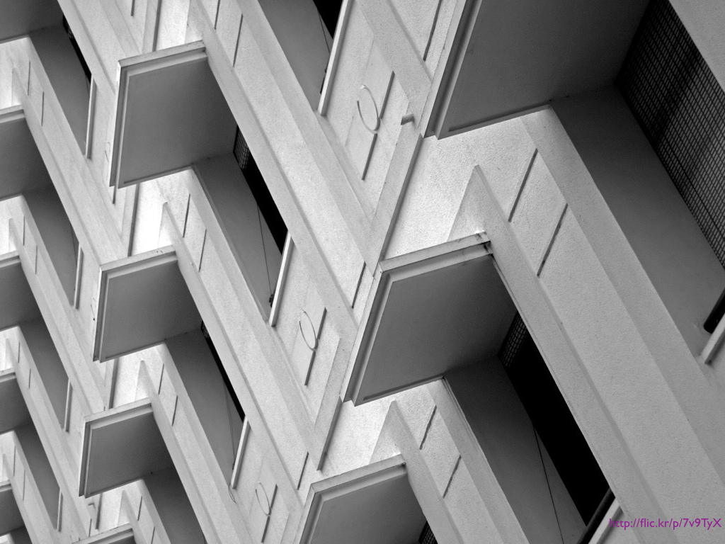 A photograph of the side of a building which has a series of repeating windows and overhangs.